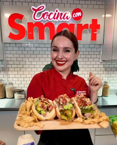 Chef Alejandra Alcalá sonriendo con una charola de hot dogs en la cocina de Cocina con Smart